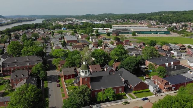 A forward aerial establishing shot of a Pennsylvania small town's business and residential districts. Ohio River in the distance. Pittsburgh suburbs.  	