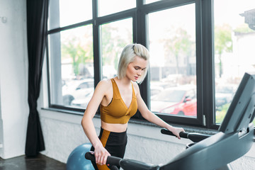 Fototapeta premium side view of young sportswoman running on treadmill at gym