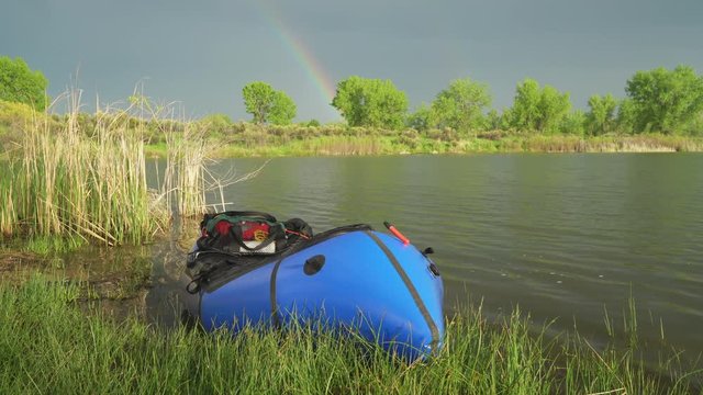 Packraft (one-person light raft used for expedition or adventure racing) on a lake shore in spring scenery with a rainbow