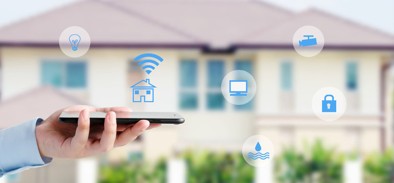 Hand using smart phone as smart home control over blur house background, smart home control concept