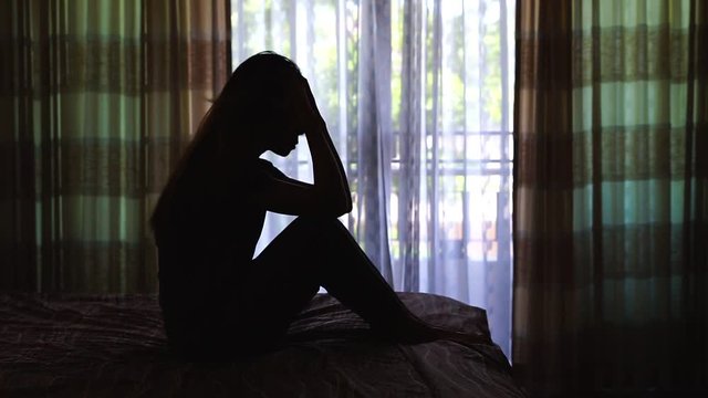 Woman Suffering From Depression Sitting On Bed in the dark bedroom