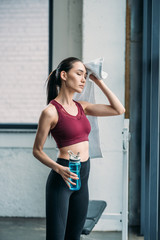 Fototapeta na wymiar tired asian sportswoman with towel and water bottle after workout at gym