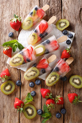 Freshly prepared popsicles ice with fresh strawberries, kiwi and blueberries on a stick close-up. Vertical top view