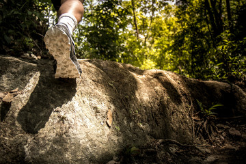 Athlete's foot wearing sports shoes on a challenging dirt track. Man trail running on rocky terrain outdoors. Close up.