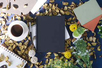 Notepad and coffee on rustic blue background with dry flower petals. Rustic nostalgia.