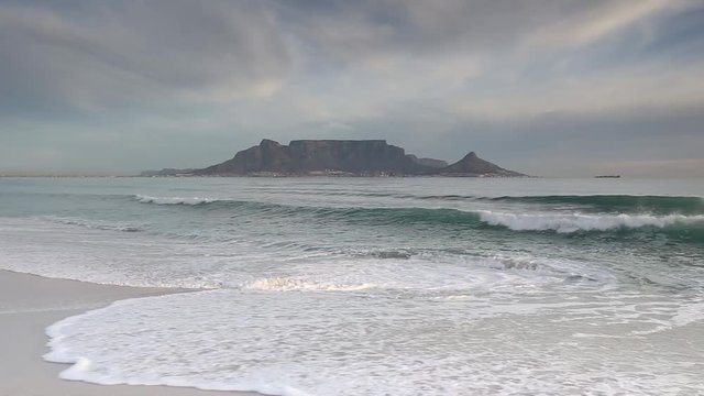 Waves crashing on a beach with table mountain in the background waves fill frame as they wash ashore