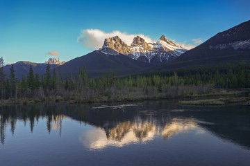 Scenic Landscape View of Snowcapped Three Sisters Mountain reflected in calm water, Alberta Foothills Canadian Rockies