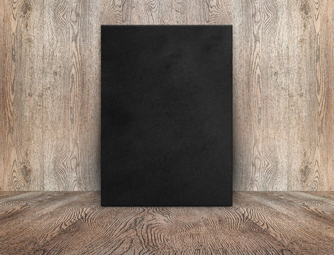 Blank black canvas poster leaning at wood wall on wooden floor in perspective room,Business mock up presentation.Template display of design or content.