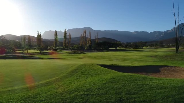 Low ground drone shot drone over a beautiful green golf course empty with trees and mountains in South Africa