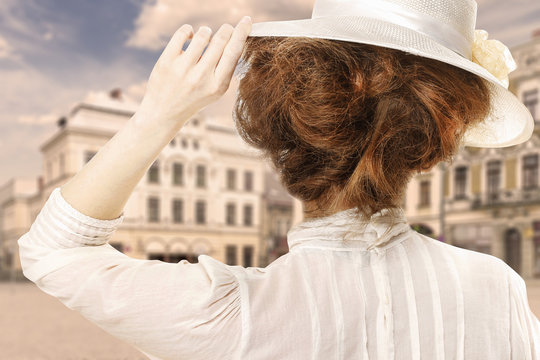 Retro styled picture of woman in victorian hat looking at the city street in Europe
