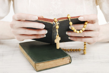 Woman holding Holy Bible and wooden rosary.