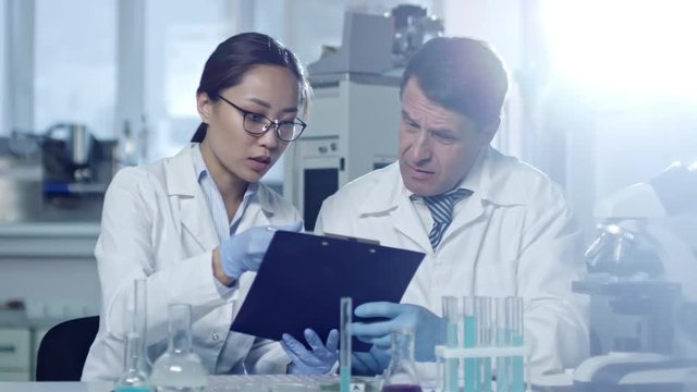Medium shot of two scientists, man and woman, analyzing data they have on clipboard when conducting research in laboratory
