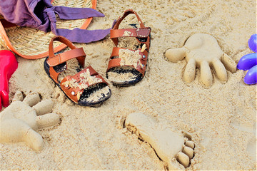 Fototapeta na wymiar Sand on the beach or in the sandbox and footprints in the sand. Form for sand and children's shoes nearby. Nearby accessories to protect the sun rays of parents. Background image for copy space.
