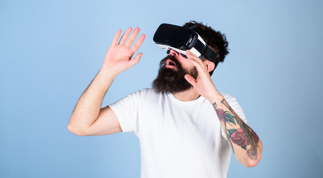 Man with beard in VR glasses, light blue background. VR gadget concept. Guy with head mounted display interact in virtual reality. Hipster on busy face exploring virtual reality with modern gadget