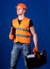 Man in helmet, hard hat holds toolbox and folder with documents, blue background. Worker, repairer, builder on dreamy face carries case with tools. Repairman ready to work. Repair service concept.