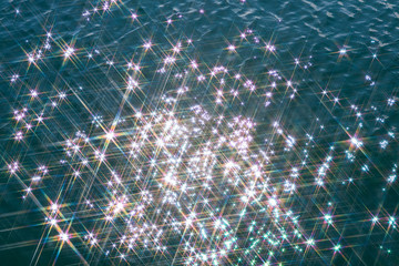 Glare on the water in the form of stars. Natural abstract sea water background.