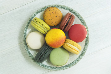 Sweet and colorful french macaroons in dish on wood table. Top view.