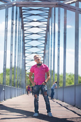 Cute emotional man with headphones in glasses in a pink shirt walking on a pedestrian bridge