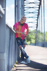 Cute emotional man with headphones in glasses in a pink shirt walking on a pedestrian bridge