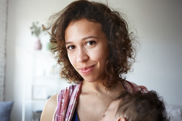 Indoor shot of beautiful young brown eyed mixed race housewife posing at home, carrying her nine...