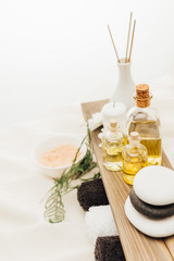 close up view of arrangement of spa treatment accessories with fern plant, towels, oil and salt on white background