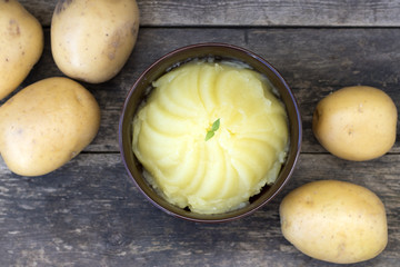 Mashed potatoes and raw potatoes side by side, located on a wooden background, rustic style
