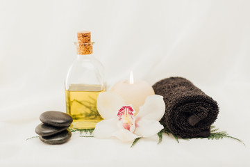Fototapeta na wymiar close up view of arrangement of spa treatment accessories with oil, towel and orchid flower on white background