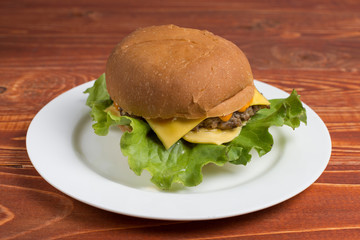 Homemade hamburger on a white plate, on a wooden table. Fast and harmful food. Without Photoshop.