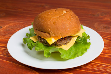 Homemade hamburger on a white plate, on a wooden table. Fast and harmful food.