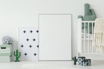 Mockup of white empty poster next to cradle in kid's room interior with cactus motif. Real photo