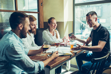 Young cheerful people smile and gesture while relaxing in pub.