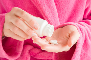 Girl in pink bathrobe. Hands holding a white bottle and pills. Receiving vitamins or medicaments. Women's issues. Medical, pharmacy and healthcare concept.