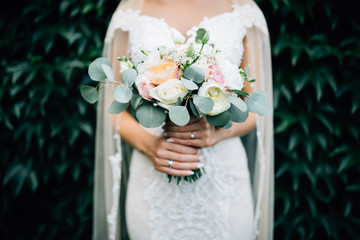 Portrait of bride in a white dress with a wedding bouquet in the hands, against a background of a green wall of plants