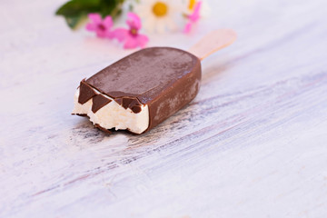 Delicious bitten classic vanilla ice cream covered whit chocolate isolated at light wooden background