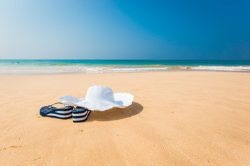 Fototapeta na wymiar hat, sun glasses and flip flops over the sand