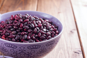 Red dry beans in a ceramic bowl on a wooden table, horizontal, copy space