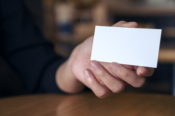 Woman's hand holding and showing an empty business card on table in office