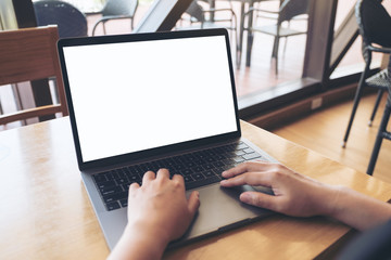 Mockup image of a hands using and typing on laptop with blank white desktop screen on wooden table in cafe