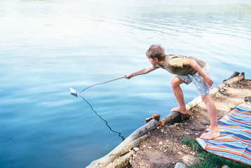 Boy launches the paper boat in lake