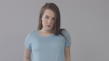 closeup portrait of young wooman posing to a camera with blowed out hair on grey