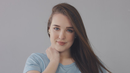 closeup portrait of young wooman posing to a camera with blowed out hair on grey