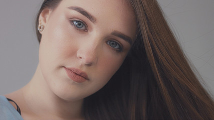 Fototapeta premium closeup portrait of young wooman posing to a camera with blowed out hair on grey