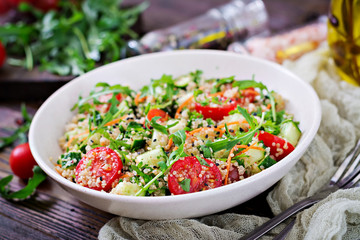 Salads with quinoa,  arugula, radish, tomatoes and cucumber in bowl on  wooden background.  Healthy food, diet, detox and vegetarian concept.