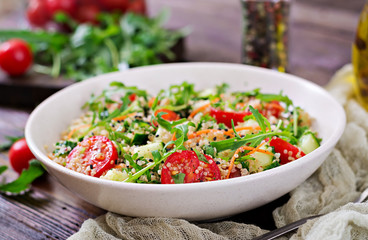 Salads with quinoa,  arugula, radish, tomatoes and cucumber in bowl on  wooden background.  Healthy food, diet, detox and vegetarian concept.