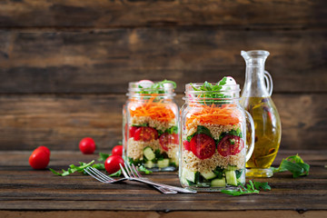 Salads with quinoa,  arugula, radish, tomatoes and cucumber in glass  jars on  wooden background.  Healthy food, diet, detox and vegetarian concept