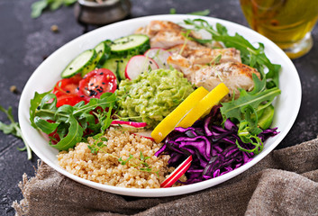 Healthy dinner. Buddha bowl lunch with grilled chicken and quinoa, tomato, guacamole, red cabbage, cucumber and arugula on gray background.