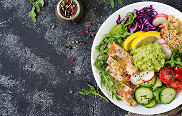 Healthy dinner. Buddha bowl lunch with grilled chicken and quinoa, tomato, guacamole, red cabbage, cucumber and arugula on gray background. Flat lay. Top view