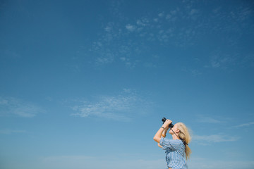 Beautiful natural blonde woman looking through binoculars against blue sky