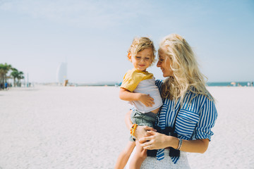 Fototapeta na wymiar Young mother and happy little son at sandy beach in Dubai, UAE