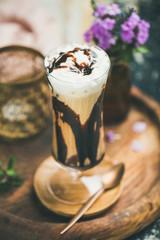 Iced mocha coffee with whipped cream, ice cream and chocolate sauce, served in tall glass over wooden textured background. Summer beverage concept